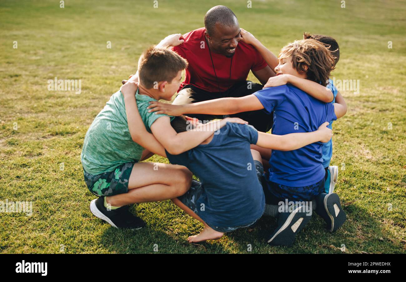 Coach and school kids huddling in a sports ground. Sports trainer