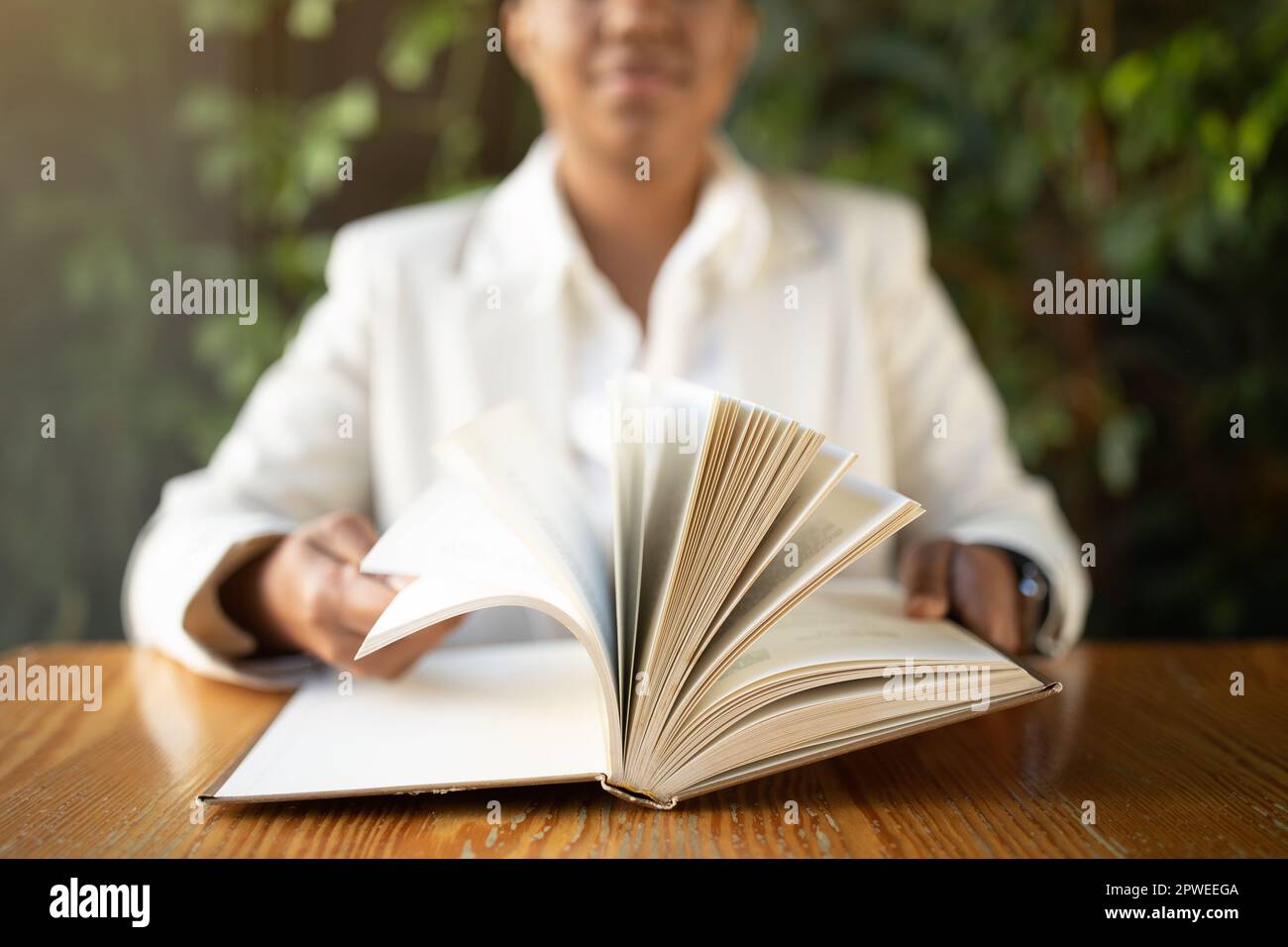 Positive young black woman in white suit sits at table, reading book in ...