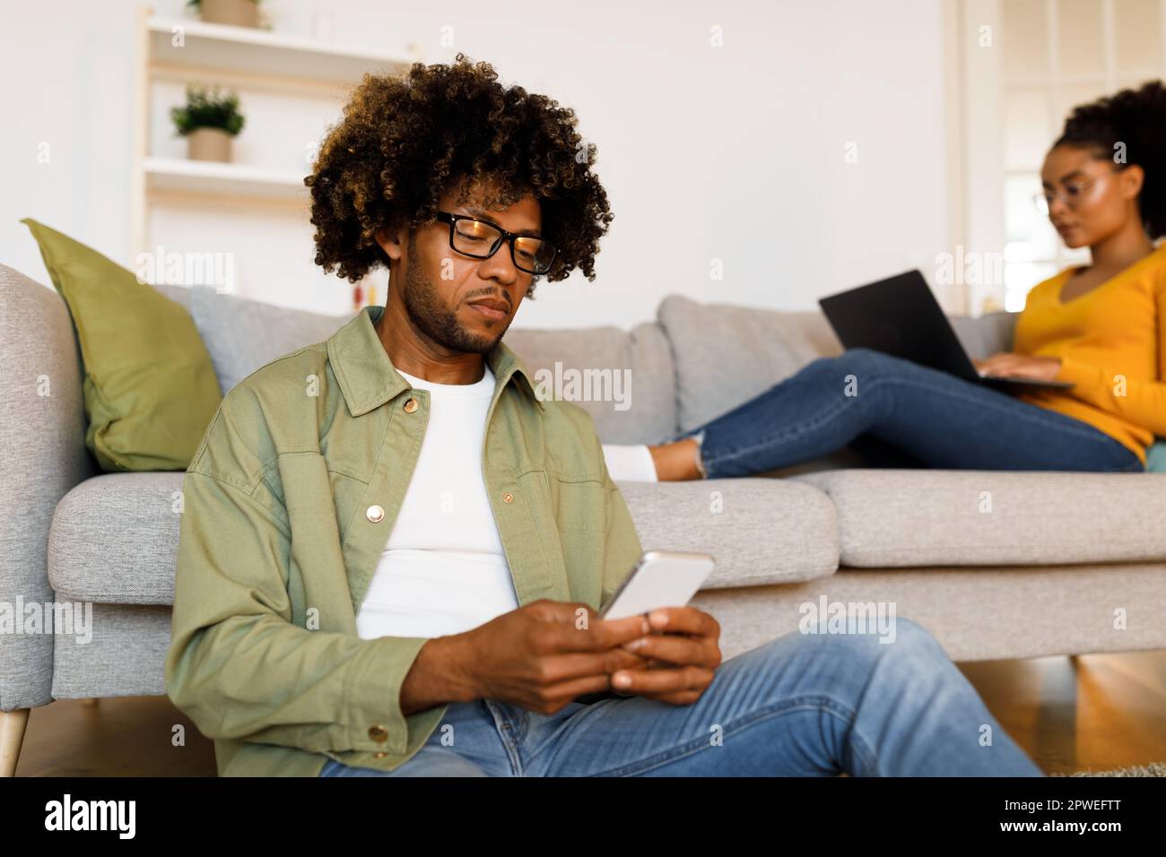 Man Using Smartphone While Wife Browsing Internet On Computer Indoor Stock Photo
