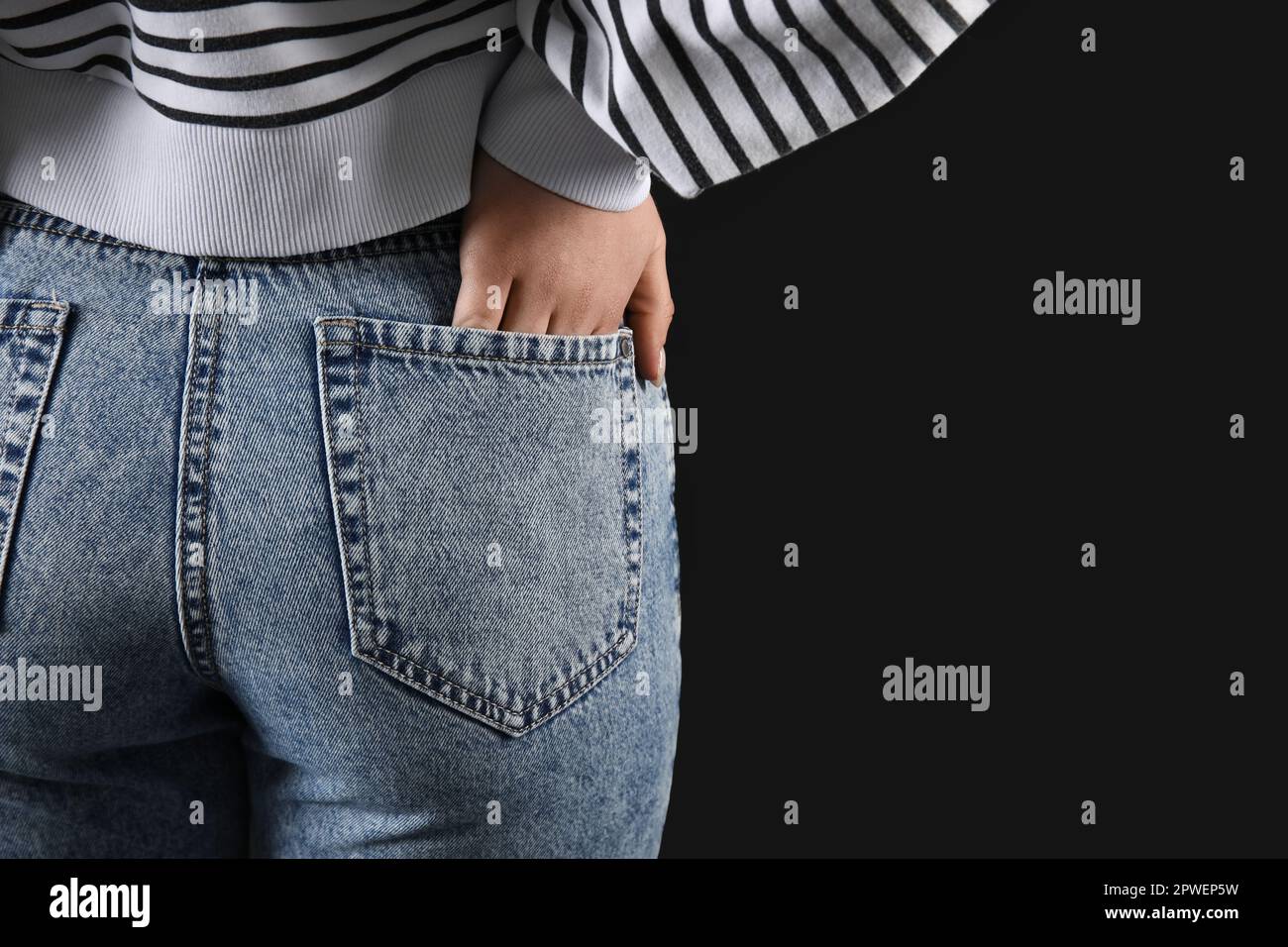 Young woman in stylish jeans on black background, back view Stock Photo ...