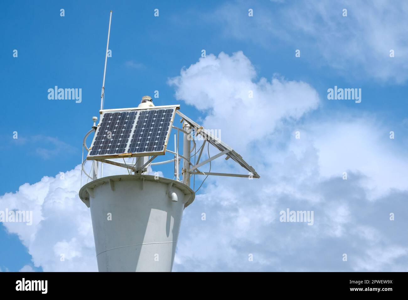 Low angle view of the lighthouse with a solar battery against clear blue sky with cirrus clouds. Alternative energy, ecology, sightseeing. Stock Photo