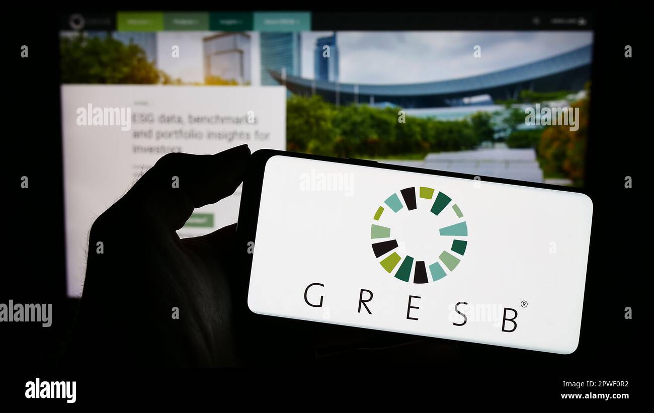 Person holding mobile phone with logo of Dutch real estate ESG foundation GRESB BV on screen in front of web page. Focus on phone display. Stock Photo