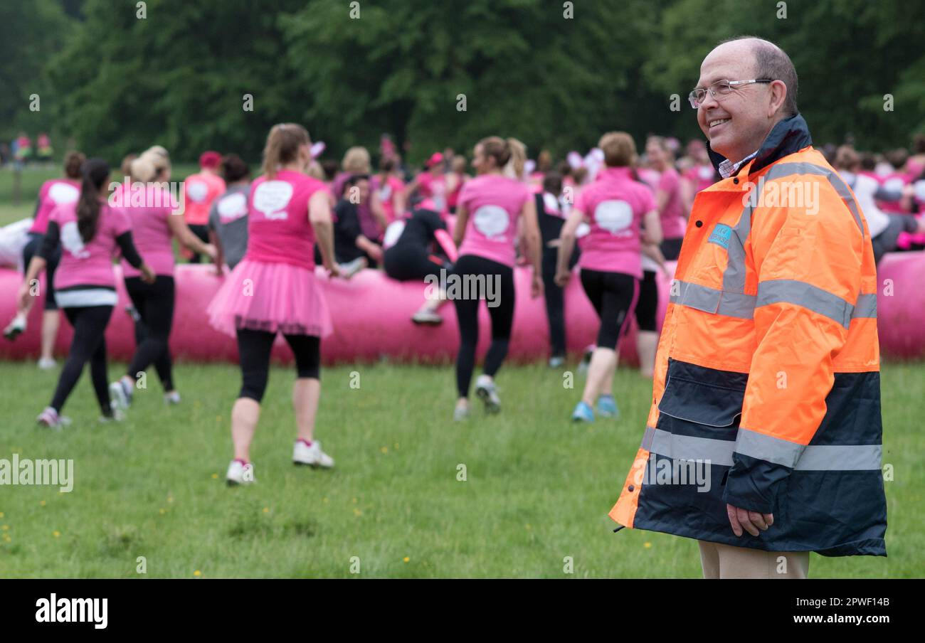 Race Steward in orange high vis jacket smiling at runners taking part in Race for Life charity event in England, June 2016 Stock Photo