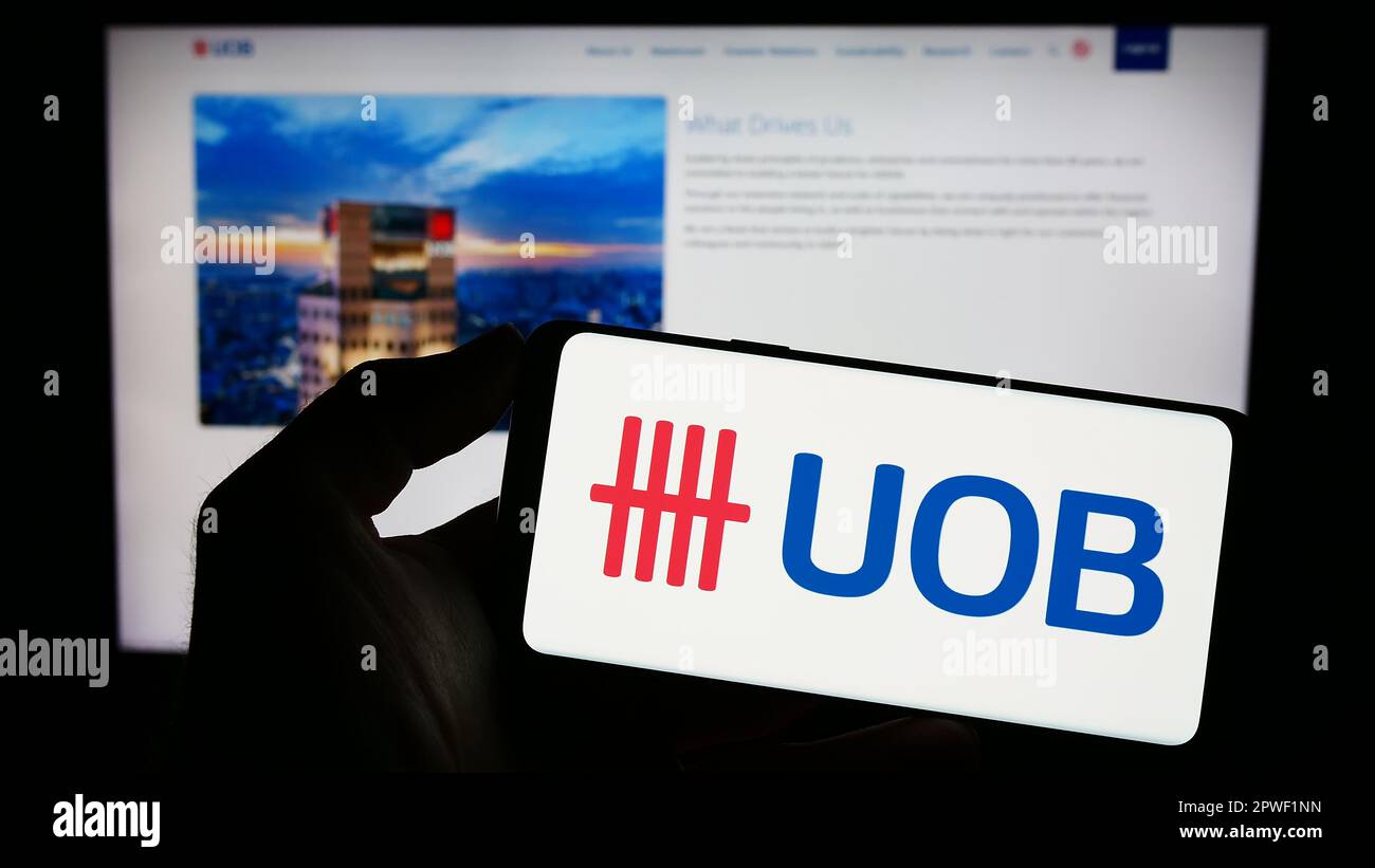 Person holding mobile phone with logo of company United Overseas Bank Limited (UOB) on screen in front of web page. Focus on phone display. Stock Photo