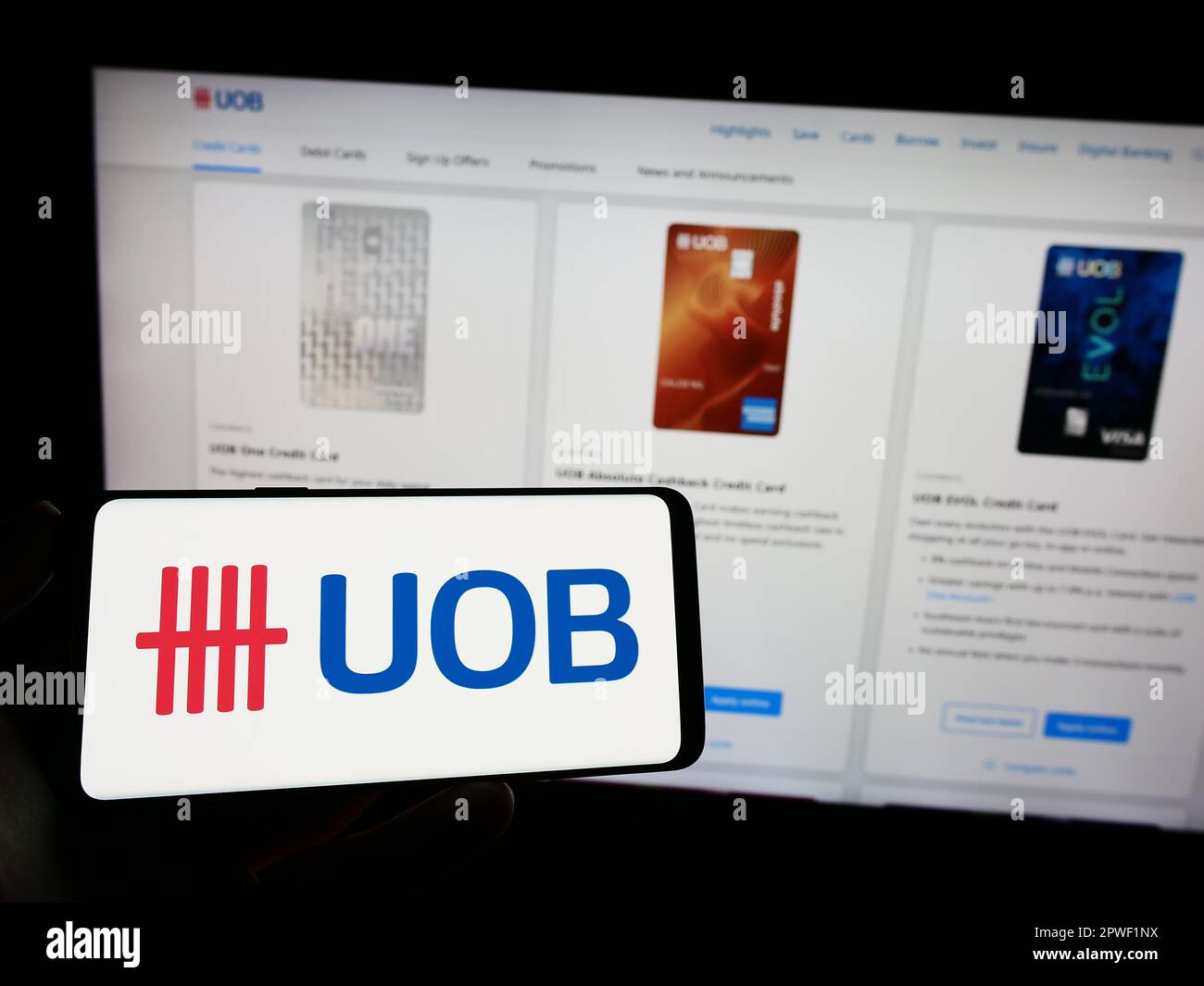 Person holding cellphone with logo of company United Overseas Bank Limited (UOB) on screen in front of business webpage. Focus on phone display. Stock Photo