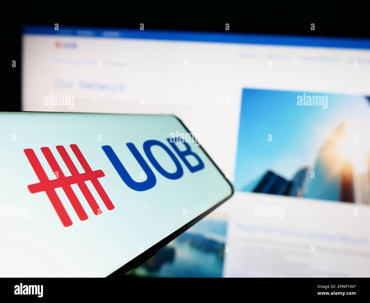 Cellphone with logo of company United Overseas Bank Limited (UOB) on screen in front of business website. Focus on center-left of phone display. Stock Photo