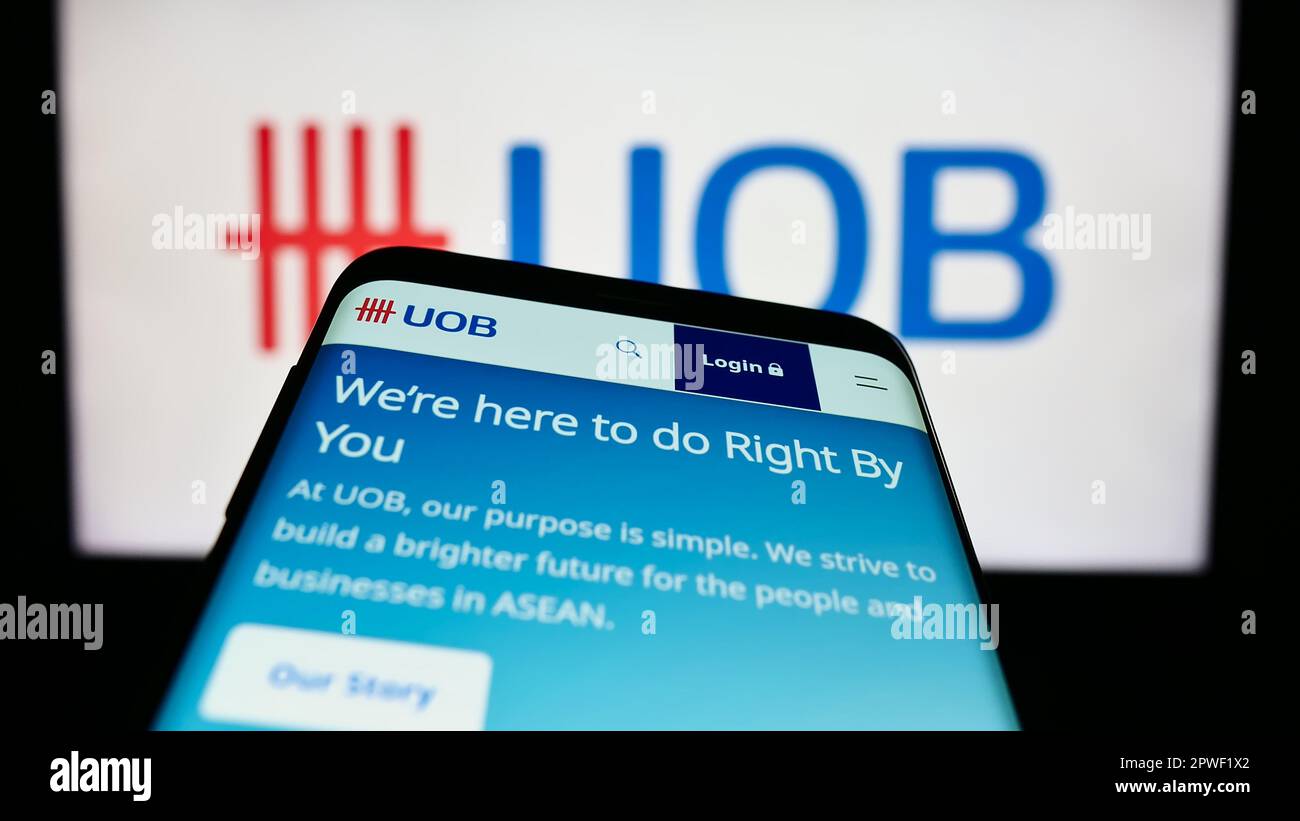 Mobile phone with website of company United Overseas Bank Limited (UOB) on screen in front of business logo. Focus on top-left of phone display. Stock Photo