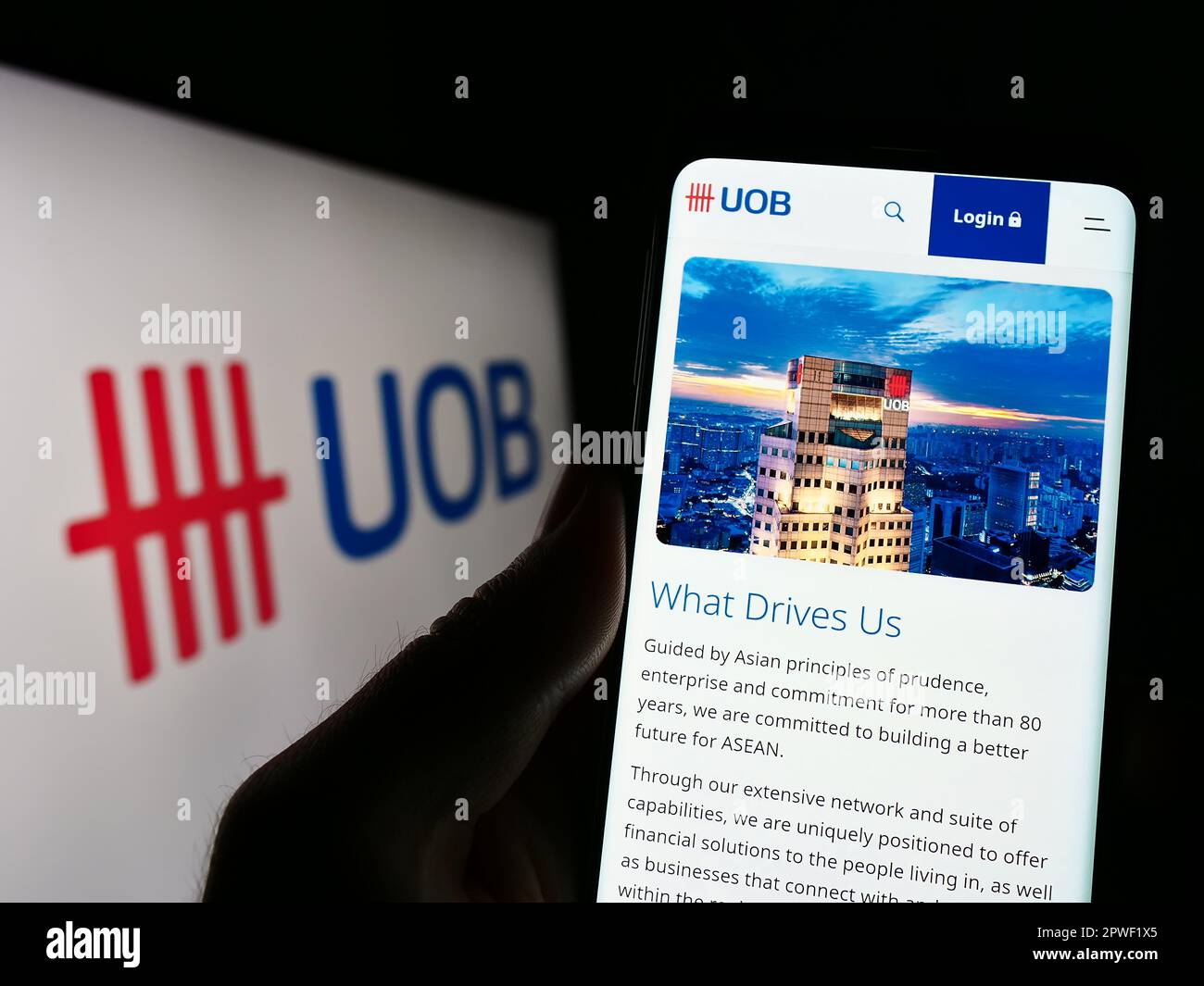 Person holding smartphone with webpage of company United Overseas Bank Limited (UOB) on screen in front of logo. Focus on center of phone display. Stock Photo