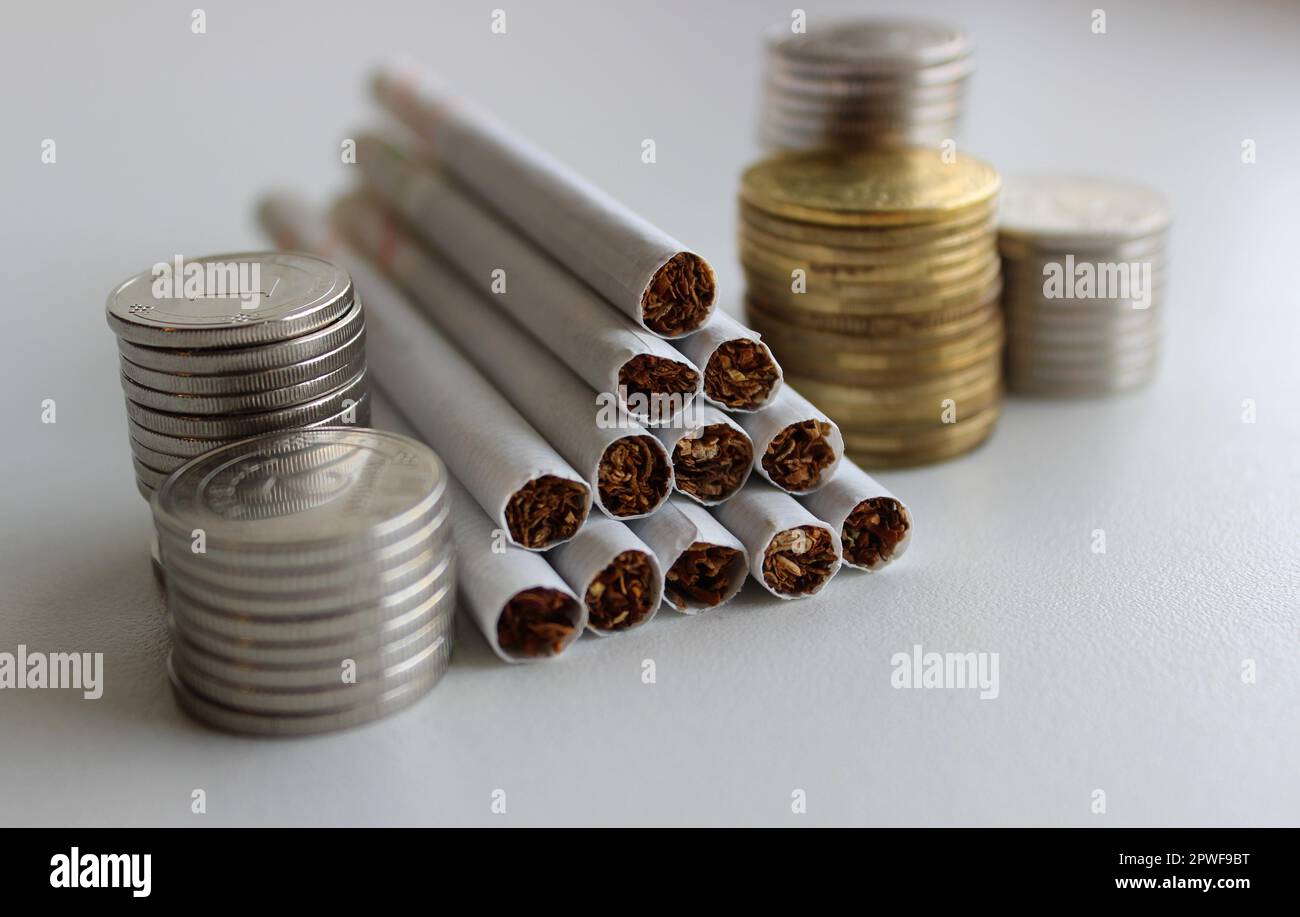 Filter cigarettes and blurred coins in a columns on a white surface ...