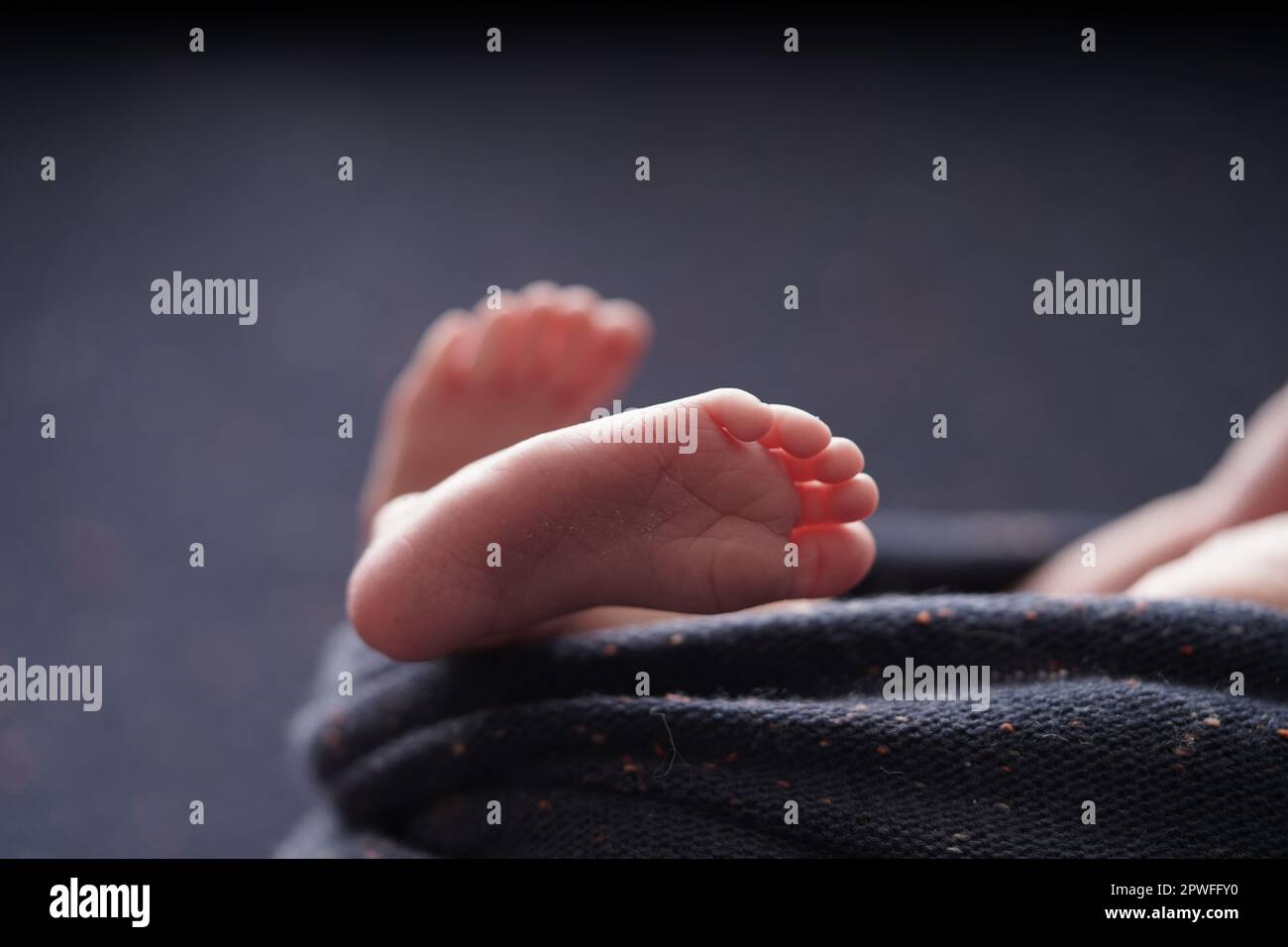 Tiny baby barefoot crossed on a navy blue background blanket. closeup