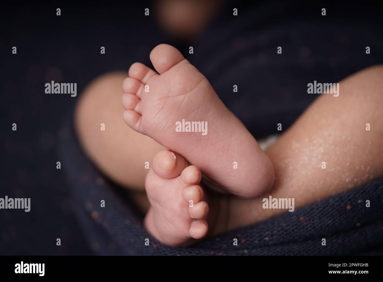 Tiny baby barefoot crossed on a navy blue background blanket. closeup