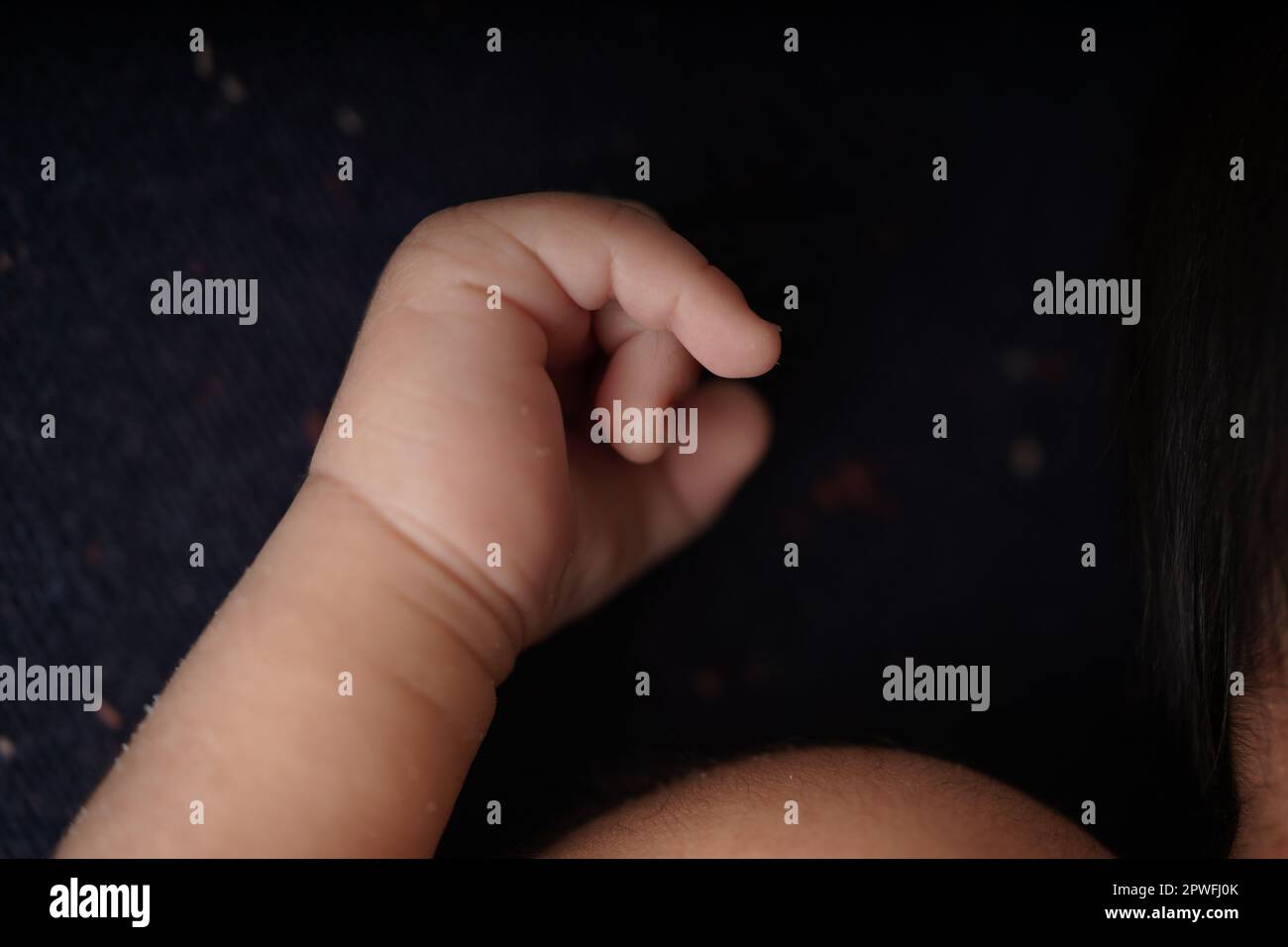 Tiny baby body and hands on navy blue background blanket. close-up view of the baby's cute hand the baby is laying comfortably in a blue blanket. Stock Photo