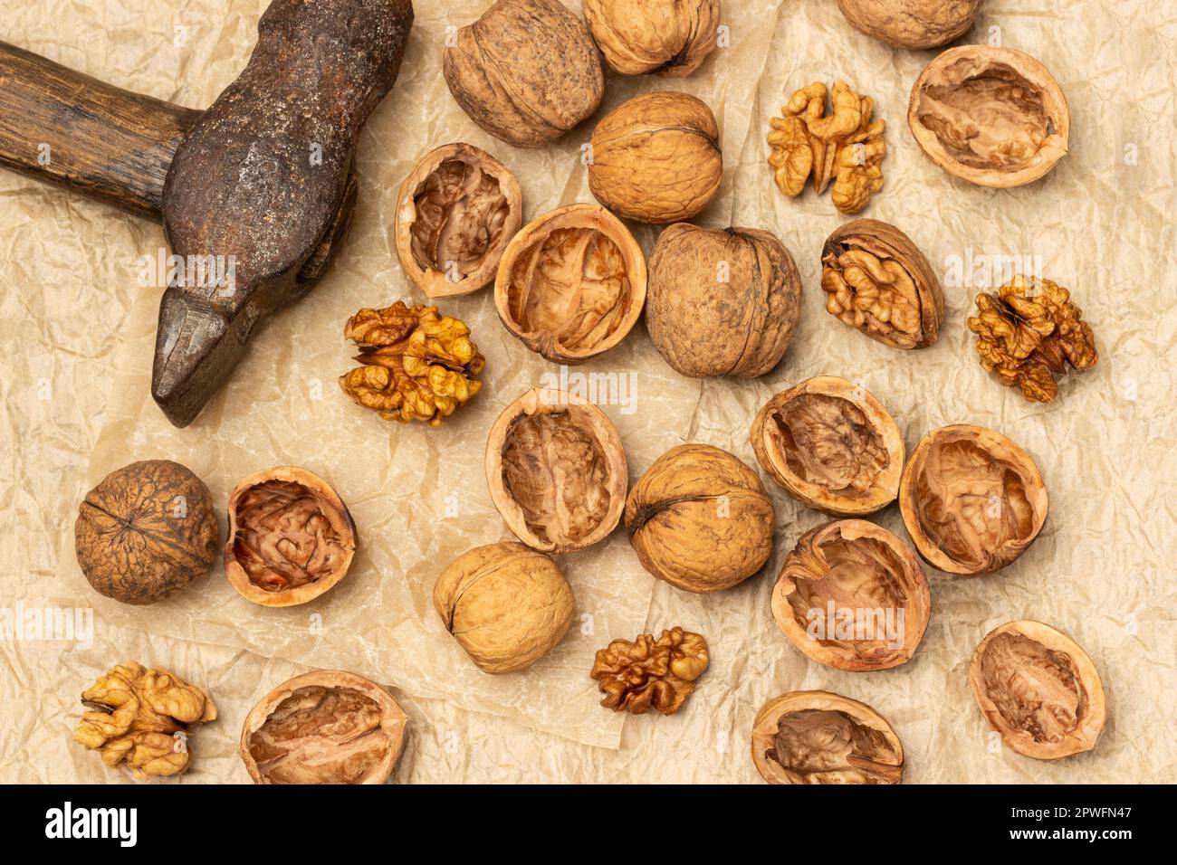 Old rusty hammer and cracked walnuts. Shells, nut kernels and whole nuts on crumpled paper. Flat lay Stock Photo