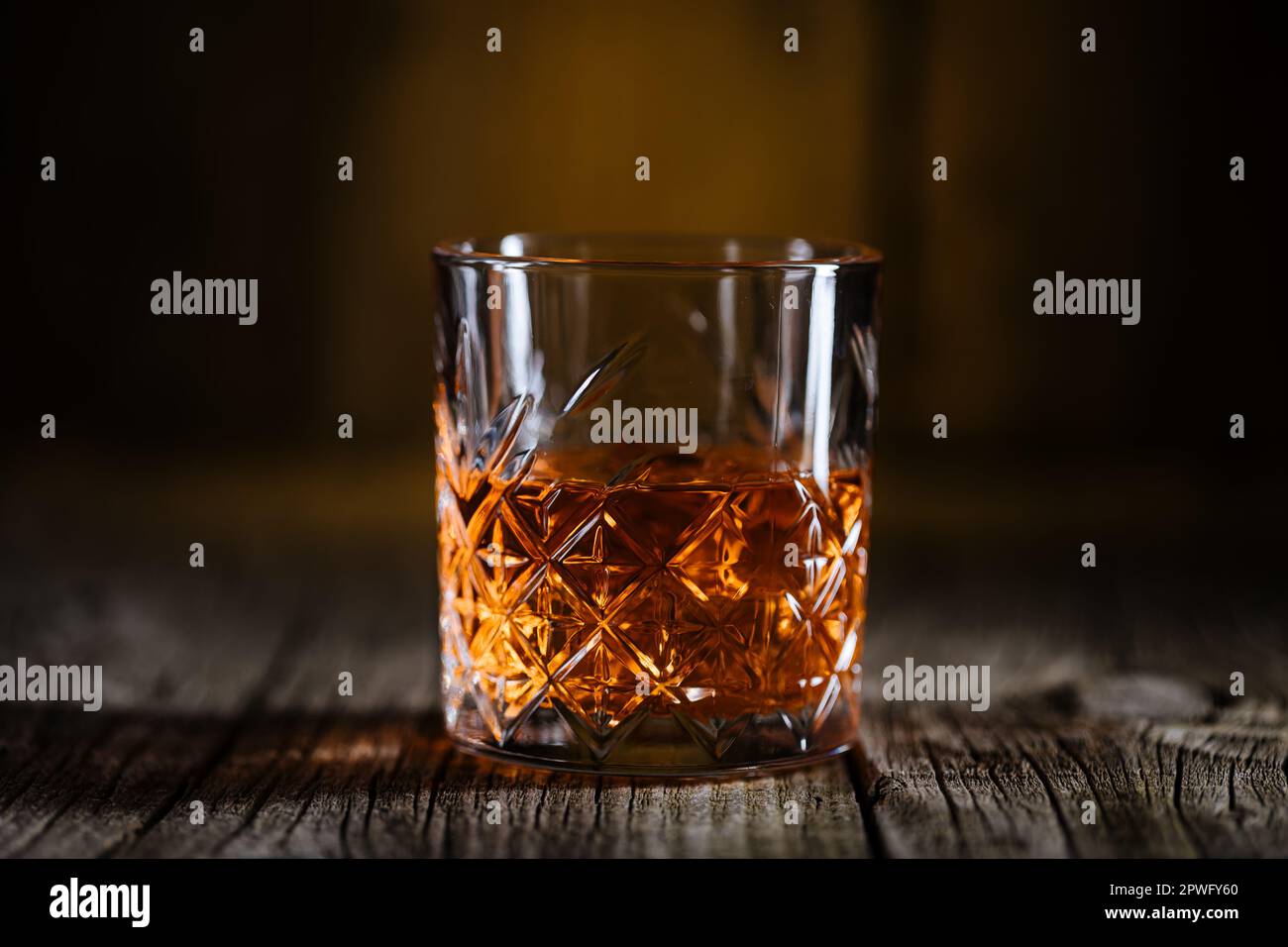 Whiskey with ice or brandy in a glass on a rustic wooden table. Whiskey with ice in a glass. Whiskey or cognac in a glass. Selective focus. Stock Photo