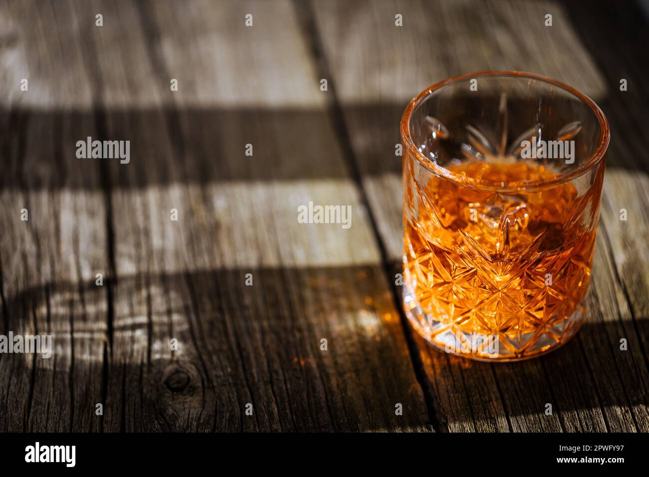 Whiskey with ice or brandy in a glass on a rustic wooden table. Whiskey with ice in a glass. Whiskey or cognac in a glass. Selective focus. Stock Photo