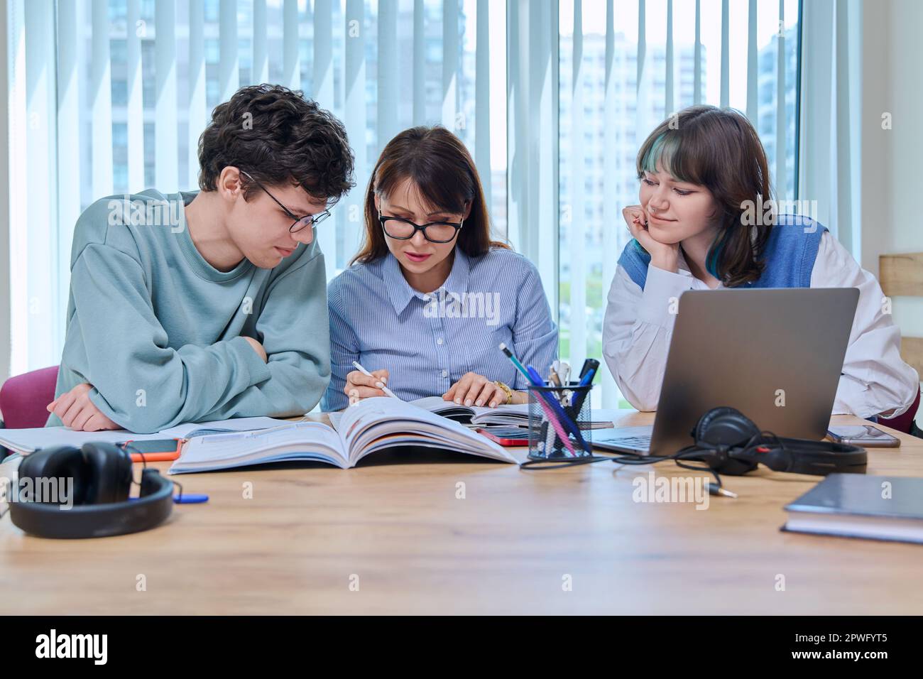 College students with teacher sitting at desk in classroom studying ...