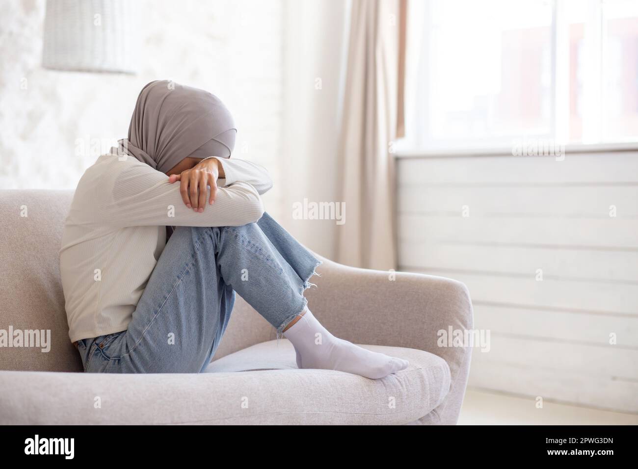 Young Muslim female student in hijab sitting on sofa at home, resting ...