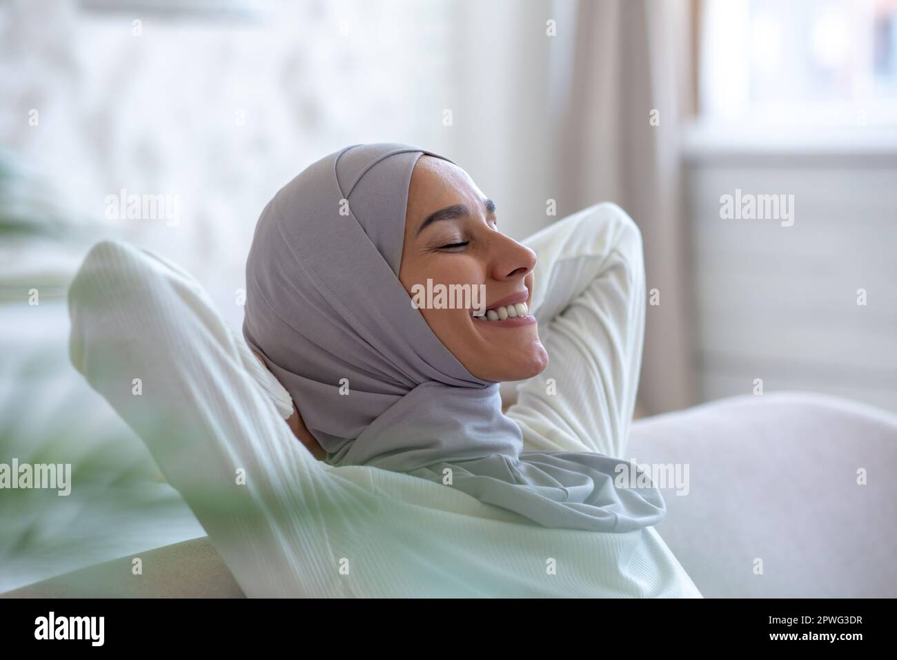 Close-up photo. Smiling Muslim young woman in hijab sitting on sofa at ...