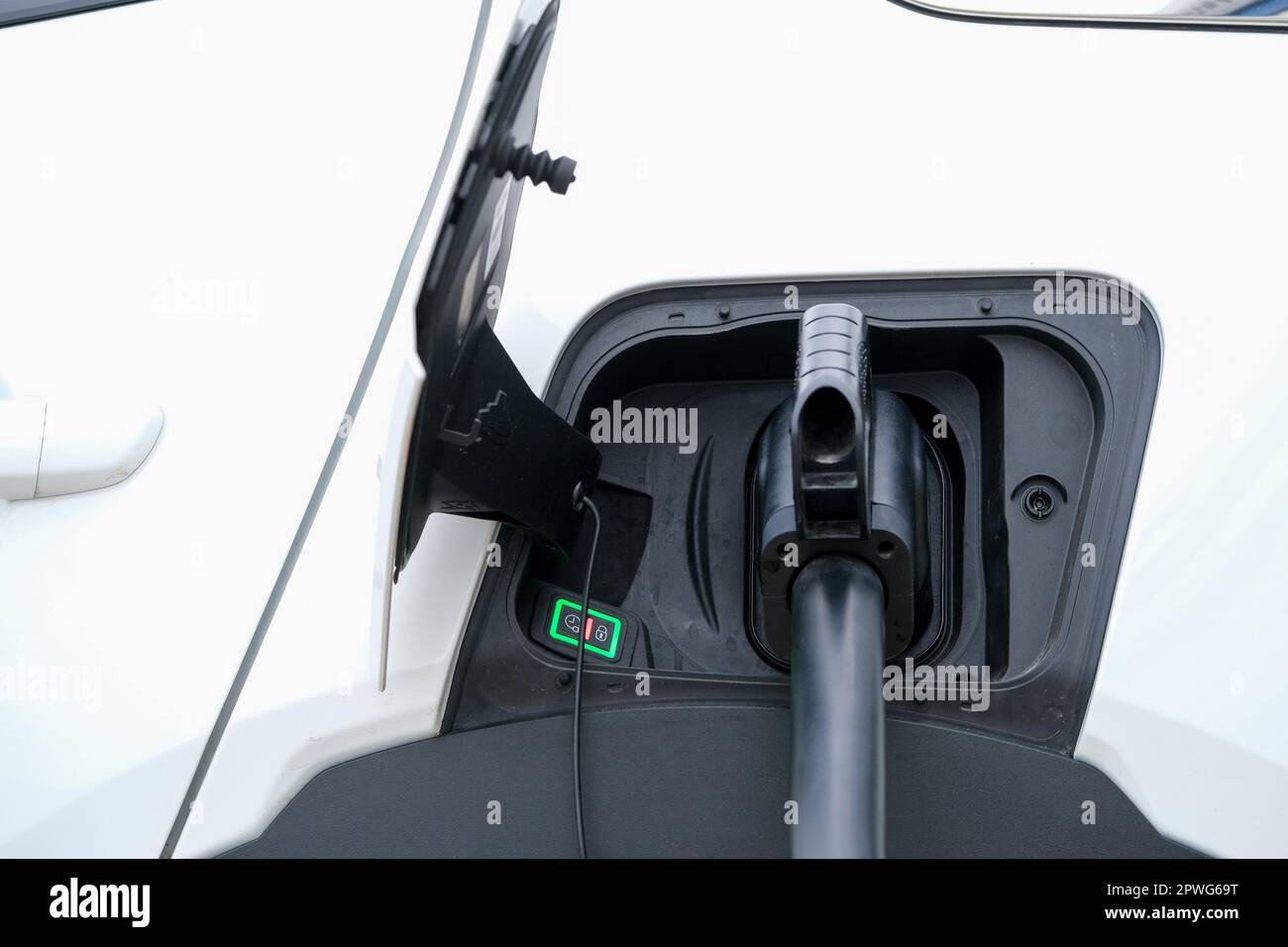 Close up charging white electric car. Electric car charging cable in jack close-up with open cover with instruction sign. Eco friendly electric car. Stock Photo