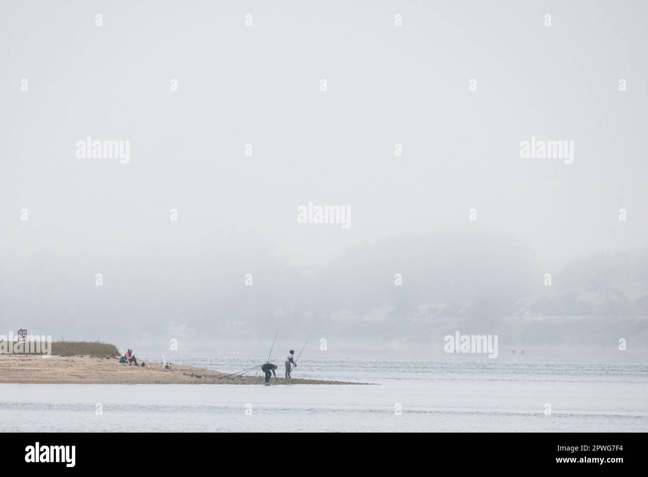 A minimalist landscape image of fishermen on a beach in California on a foggy day with lots of negative space overhead. Stock Photo