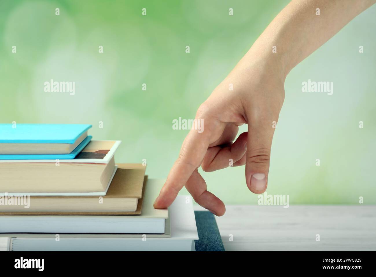 Woman climbing up stairs of books with fingers on white wooden table against blurred background, closeup Stock Photo
