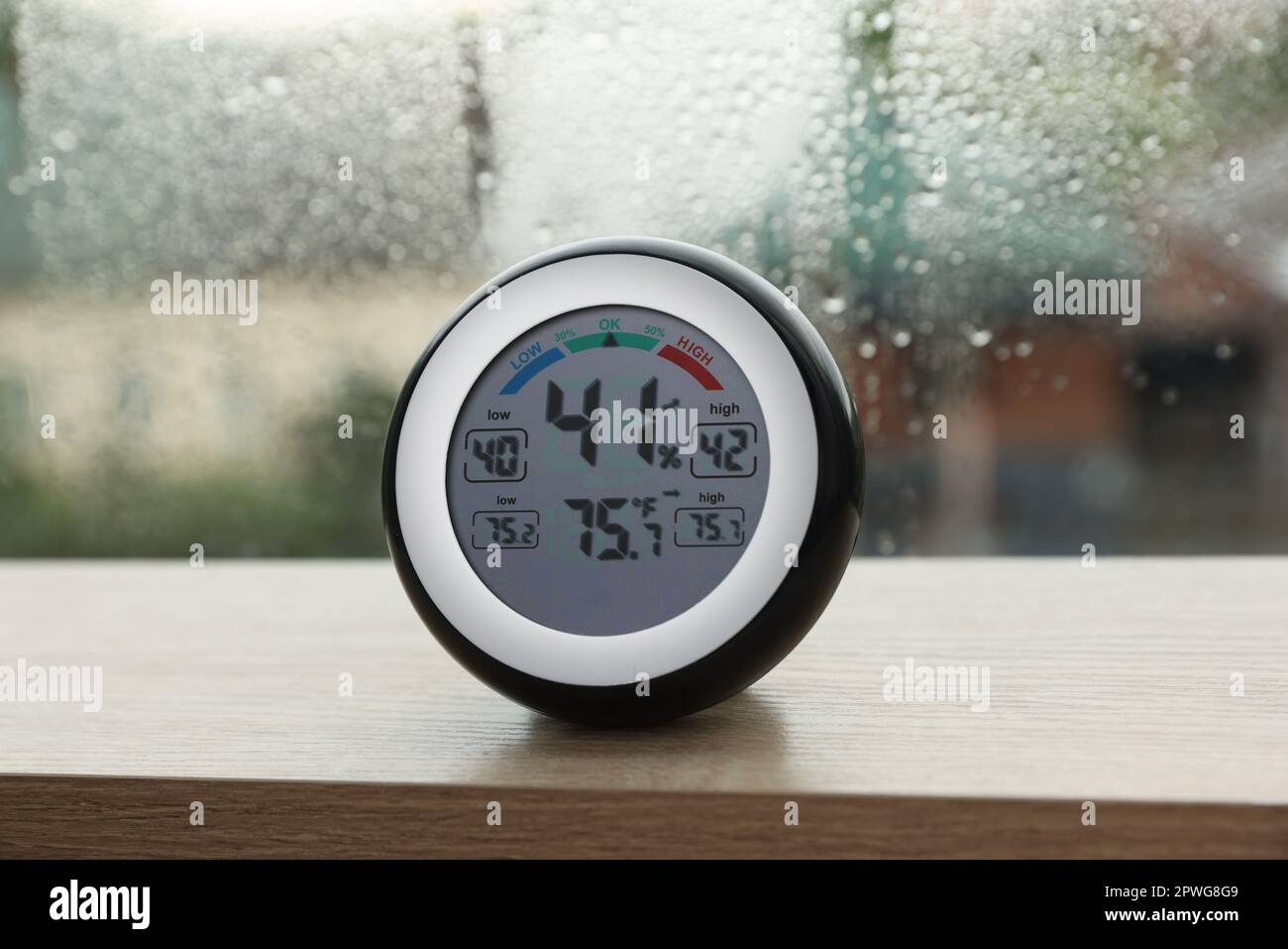 Digital hygrometer with thermometer near window on rainy day Stock