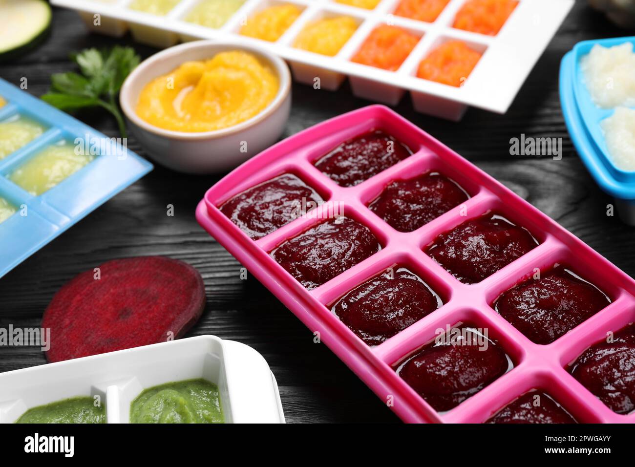 Different frozen purees in ice cube trays and ingredients of black