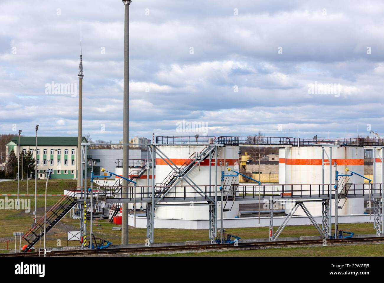 Tank farm with cylindrical fuel storage, fenced, with lightning rods, against a cloudy sky