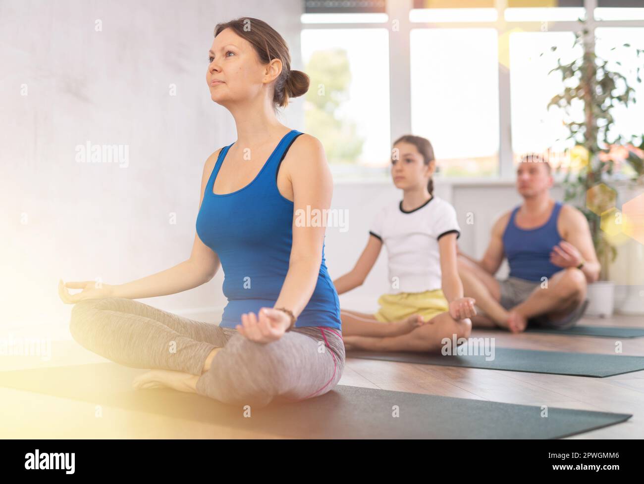 Happy middle-aged woman practicing lotus pose of yoga with her family ...
