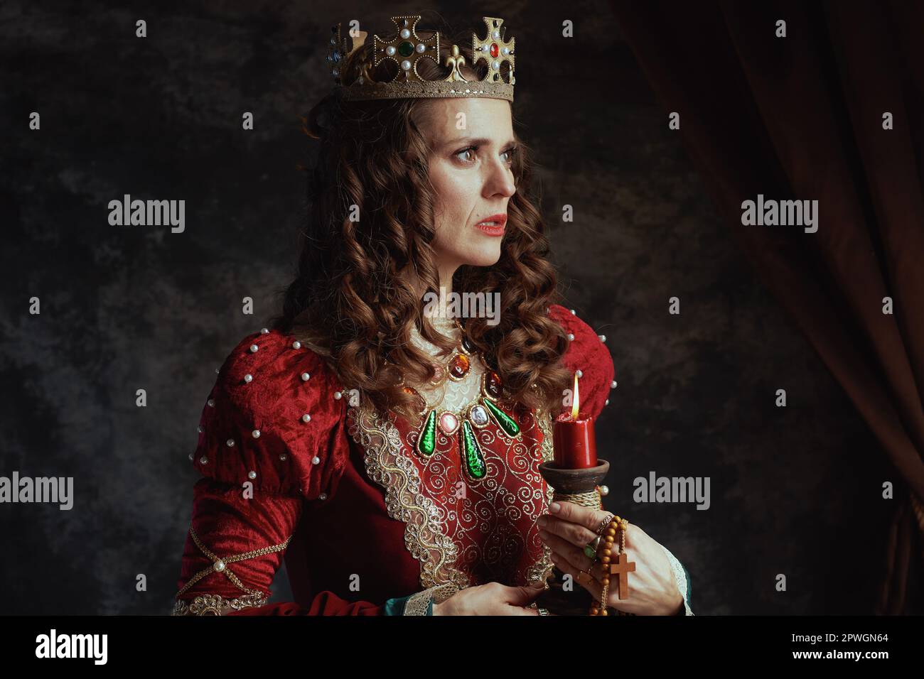 medieval queen in red dress with candle and crown on dark gray ...