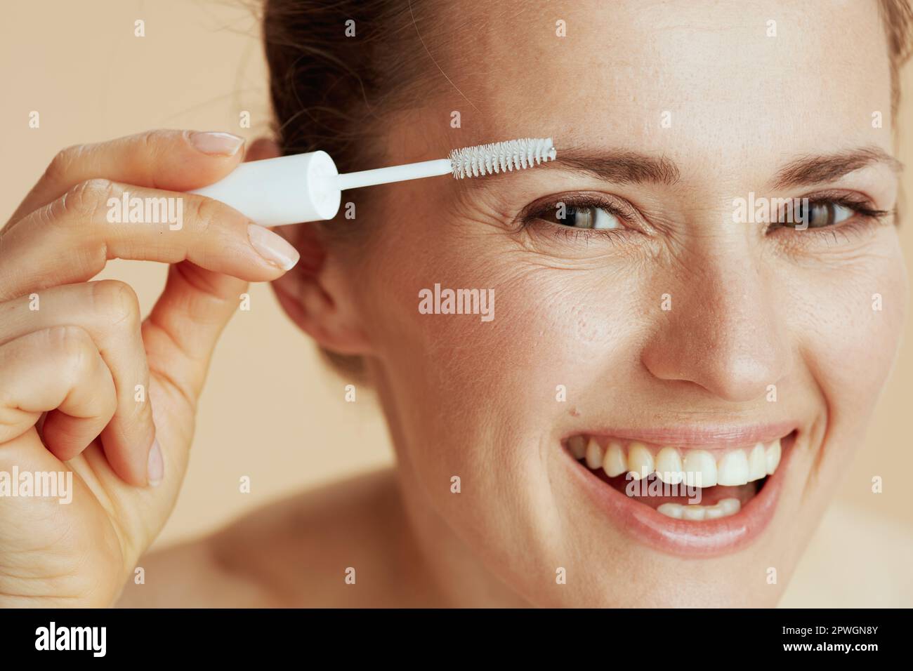smiling middle aged woman with brow brush on beige background. Stock Photo