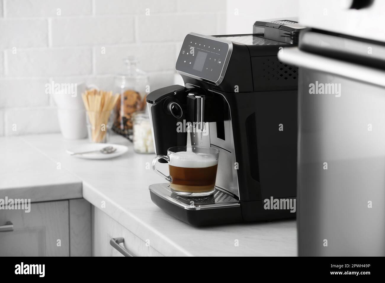 Modern electric espresso machine making coffee with milk on white marble countertop in kitchen