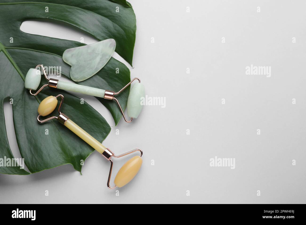 Gua sha stone, different face rollers and monstera leaf on light