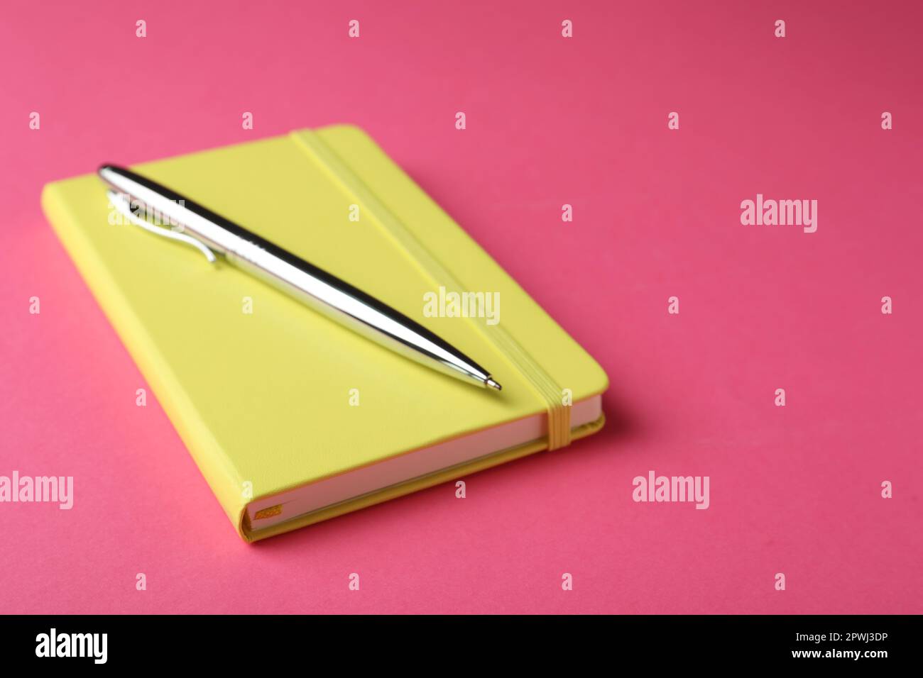 New stylish planner with hard cover and pen on pink background. Space for text Stock Photo
