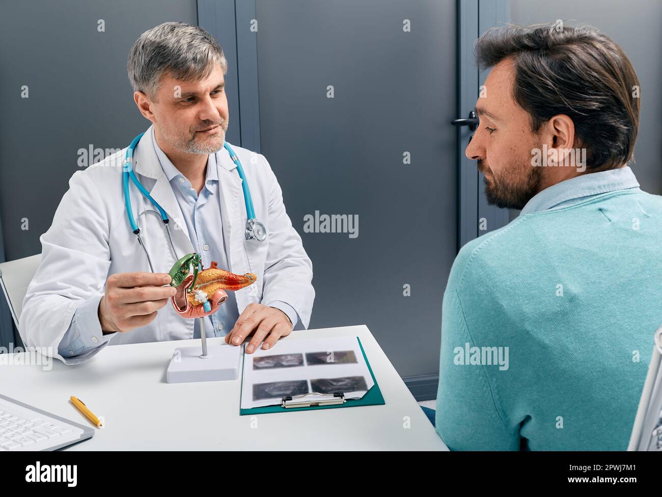 Treatment of gallbladder diseases and cholelithiasis. Gastroenterologist doctor showing gallbladder on anatomical pancreas model for male patient duri Stock Photo