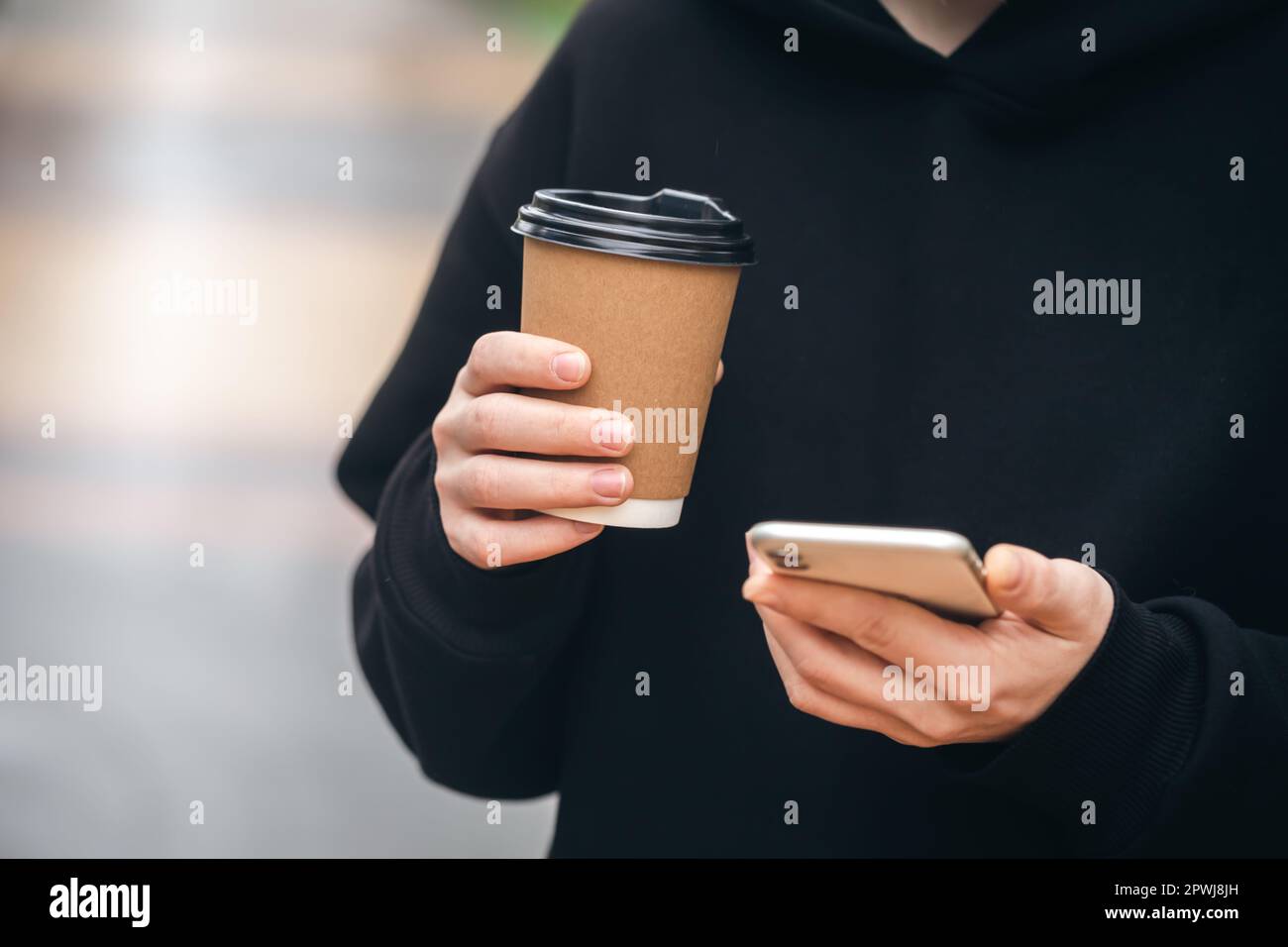 Man holding paper cup and smartphone outdoors. Stock Photo