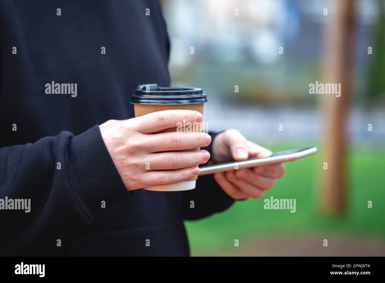 Man holding paper cup and smartphone outdoors. Stock Photo