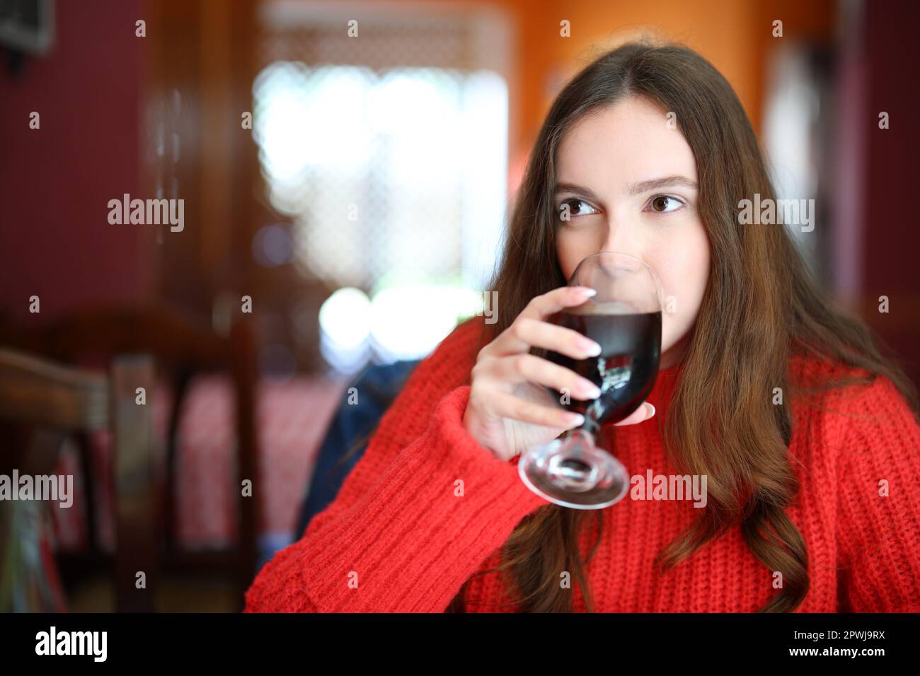 Woman in red sweater drinking soda sitting in a bar Stock Photo