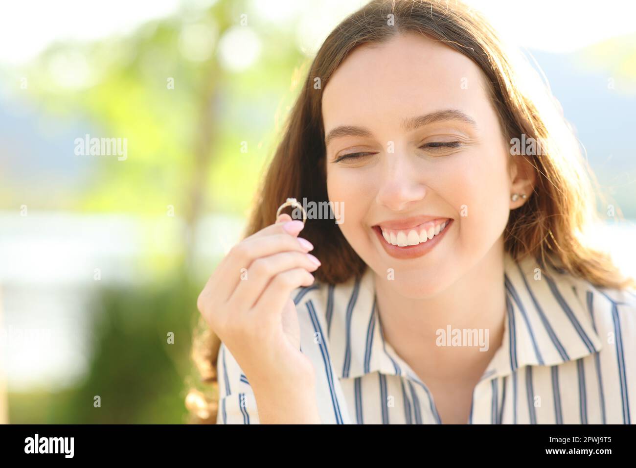 Happy fiancee looks at engagement ring outdoors in nature Stock Photo