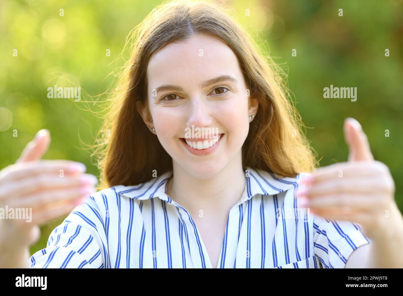 Front view portrait of a happy woman inviting to come in a park Stock Photo