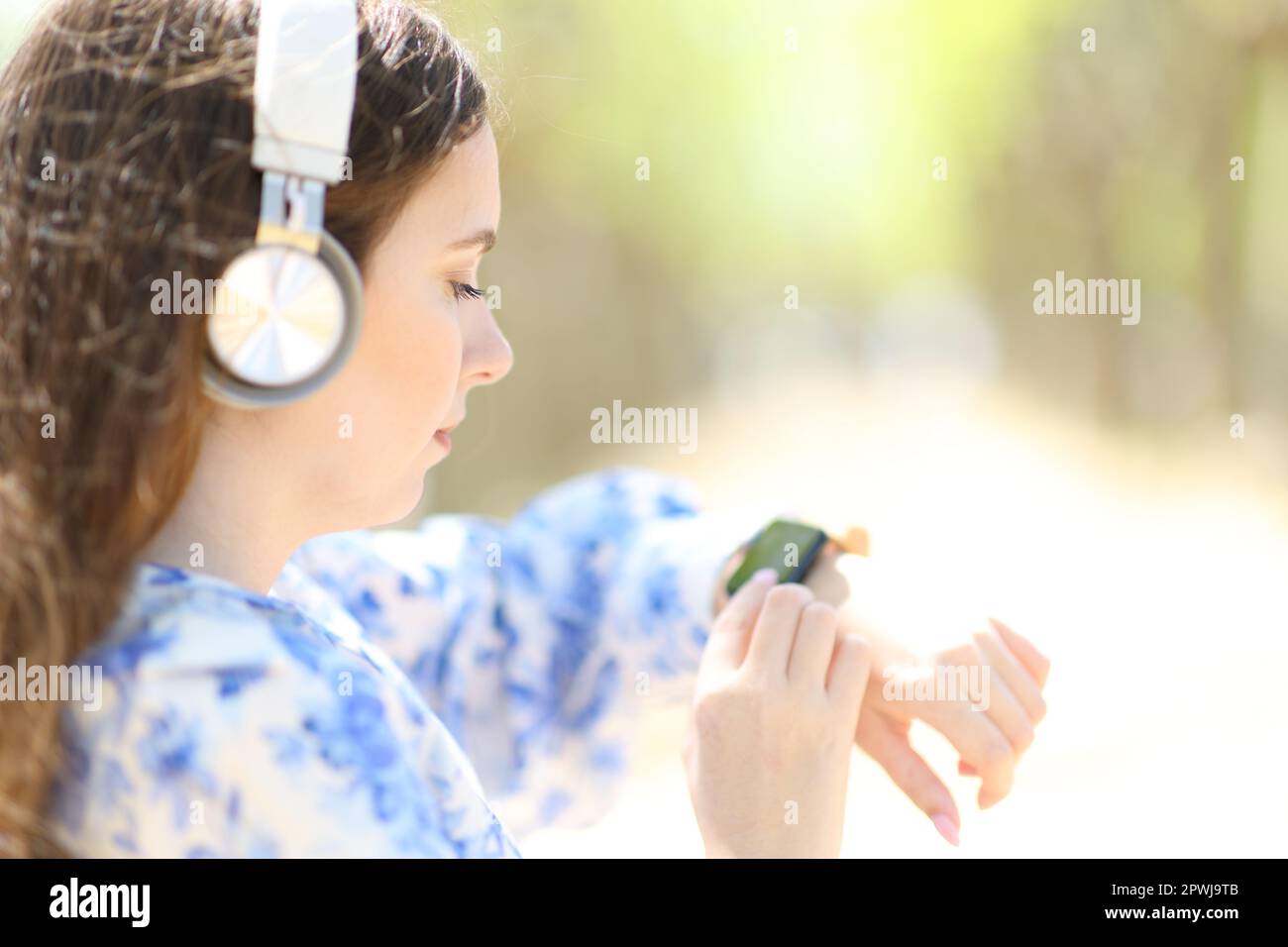 Profile of a woman listening audio with headphone using smartwatch in a park Stock Photo