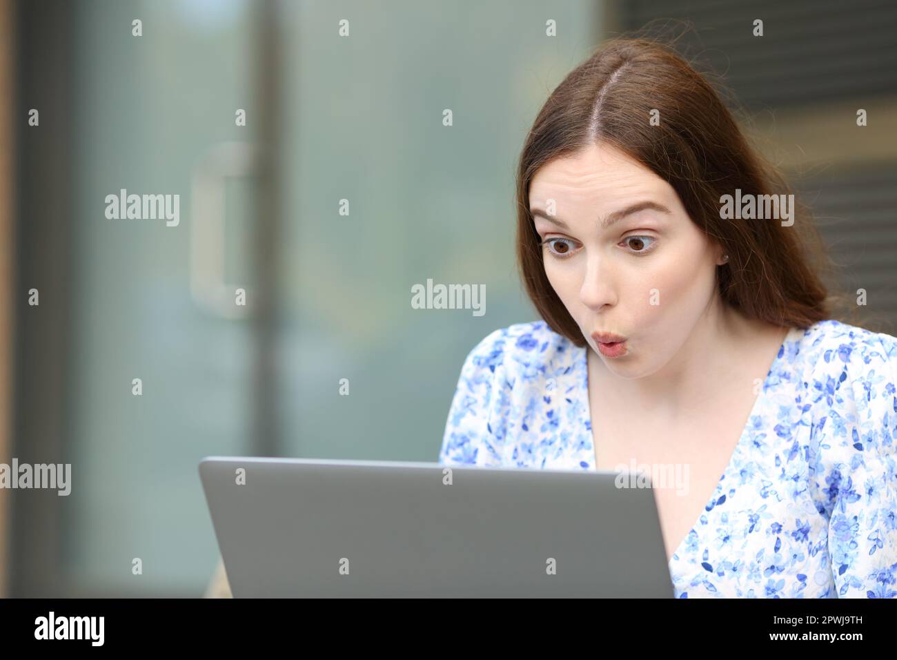 Surprised woman checks laptop sitting in the street Stock Photo