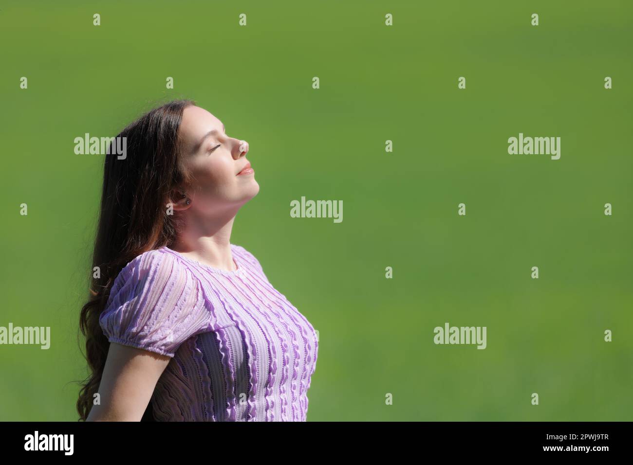 Side view portrait of a woman breathing fresh air on green background in nature Stock Photo