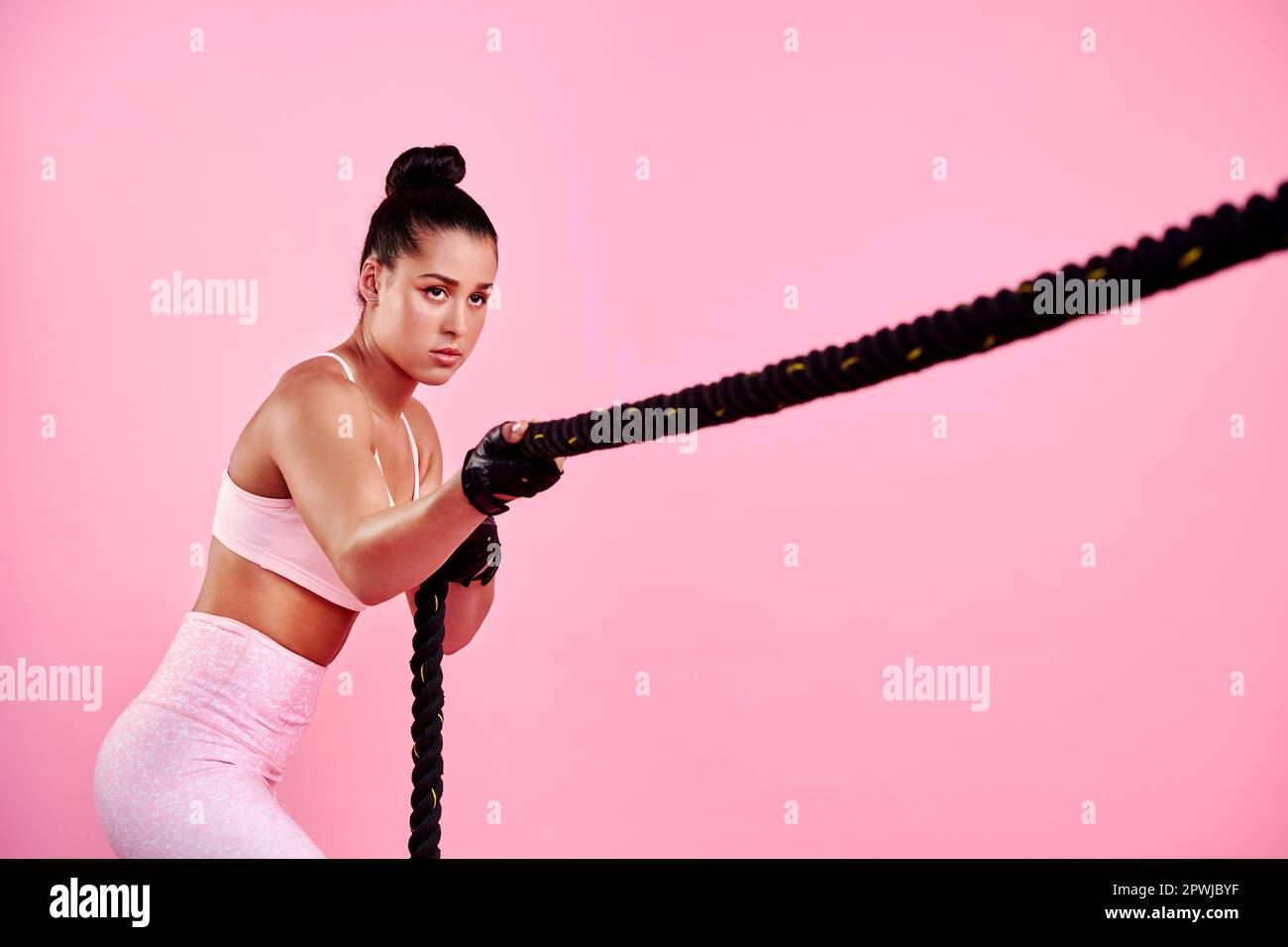 With discipline you can design a strong body. Studio shot of a sporty young woman exercising with a battle rope against a pink background Stock Photo Alamy