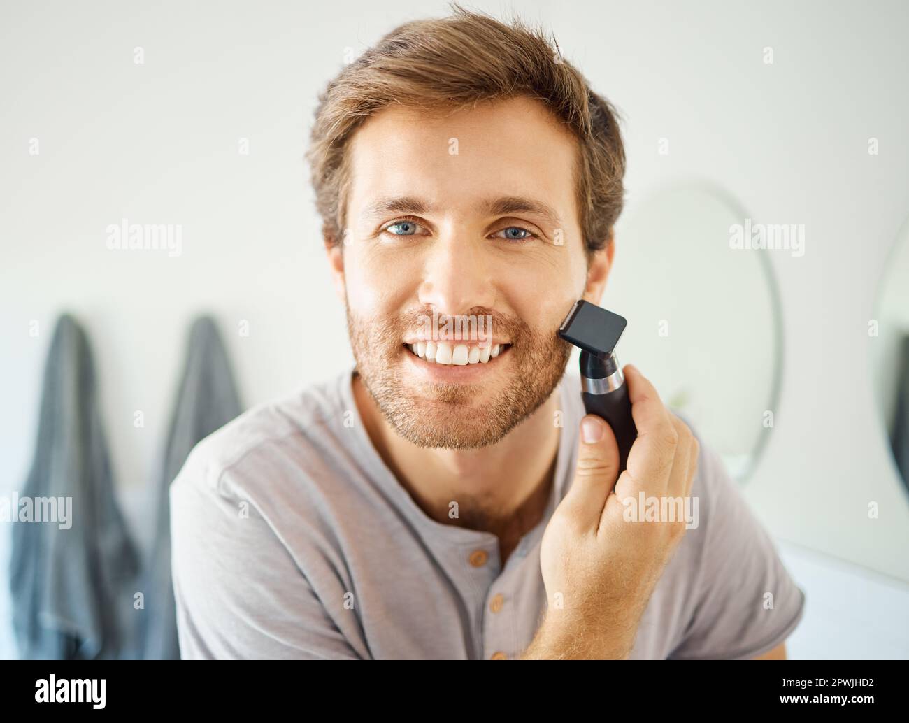 One handsome man shaving his face hair in a bathroom at home. Caucasian