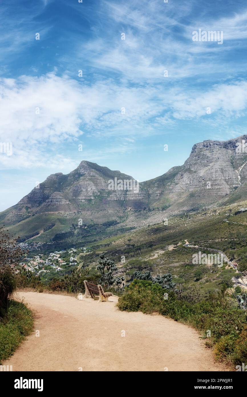 Sandy path through a landscape with mountains against a cloudy blue sky ...