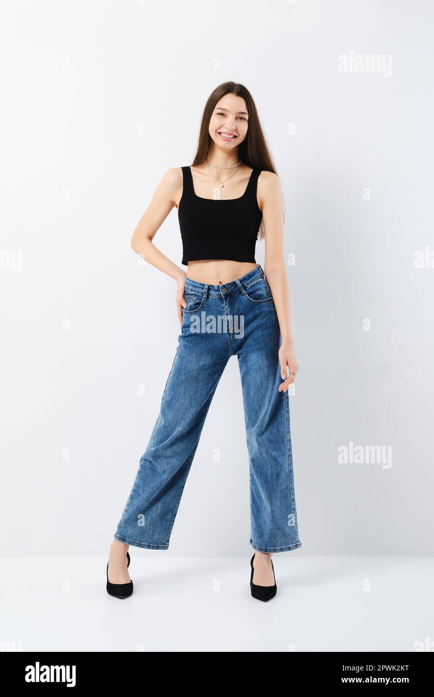 Full length portrait of young woman in black tank top and wide jeans ...