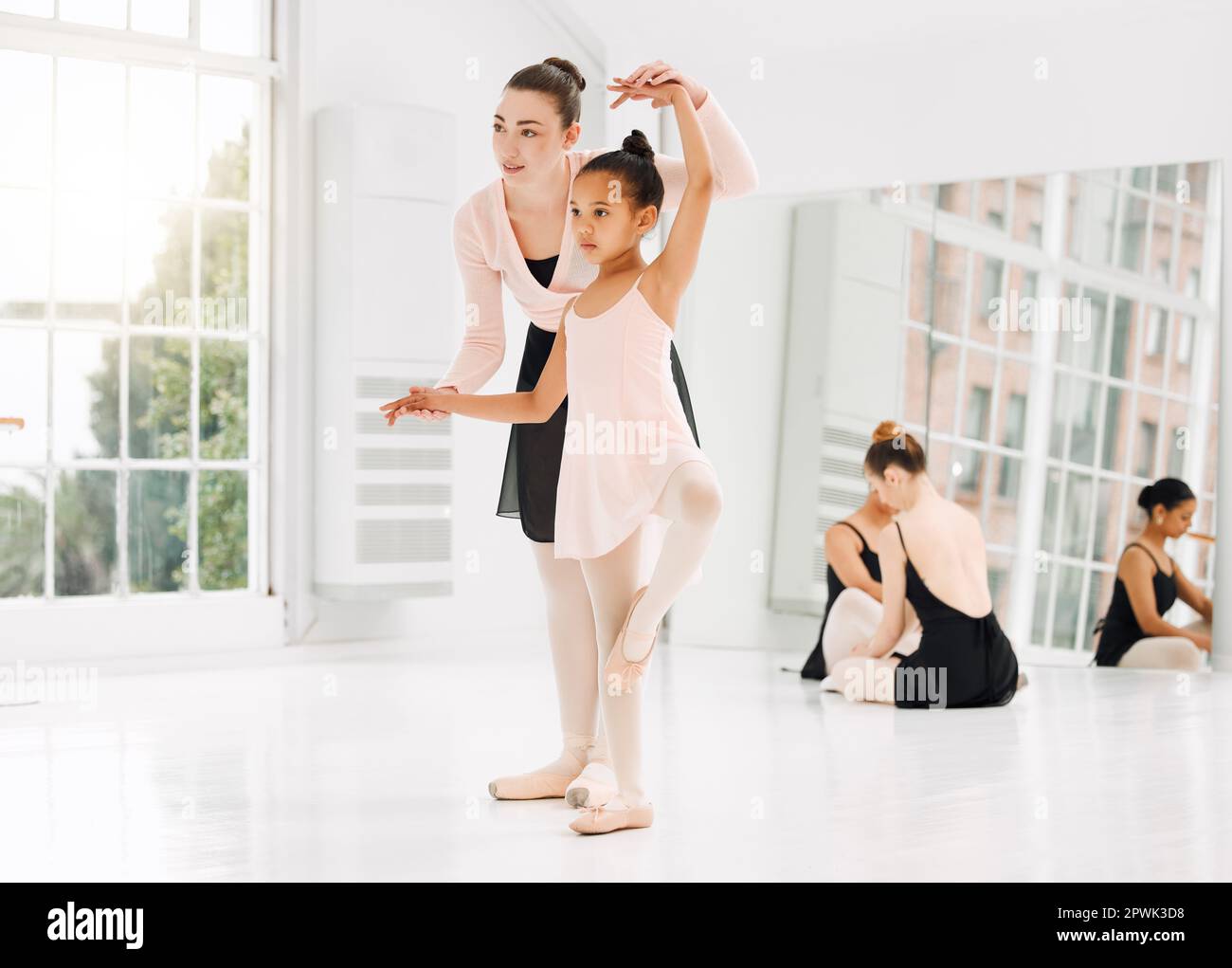 A little adorable young ballerina in black sportwear and white tights doing  stretching in the interior studio posing on camera in bright sunlight from  window Stock Photo