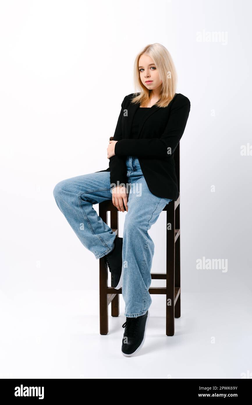 girl in tank top, jacket and jeans sits on chair in studio Stock Photo
