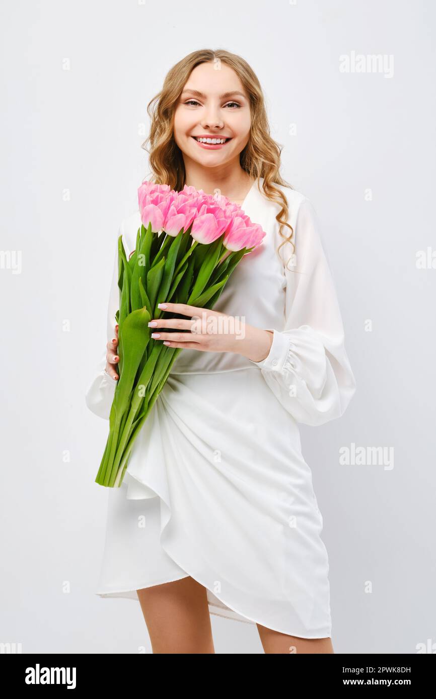 Cute young cheerful woman in white dress posing with bouquet of tulips ...
